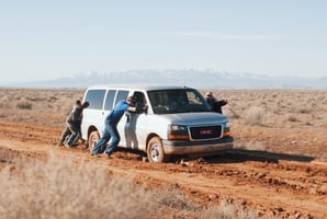 3 men trying to push a van out of the mud