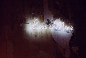 White neon sign on a black background that says Less is More