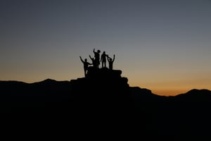 Group of people celebrating on top of a mountain at sunrise