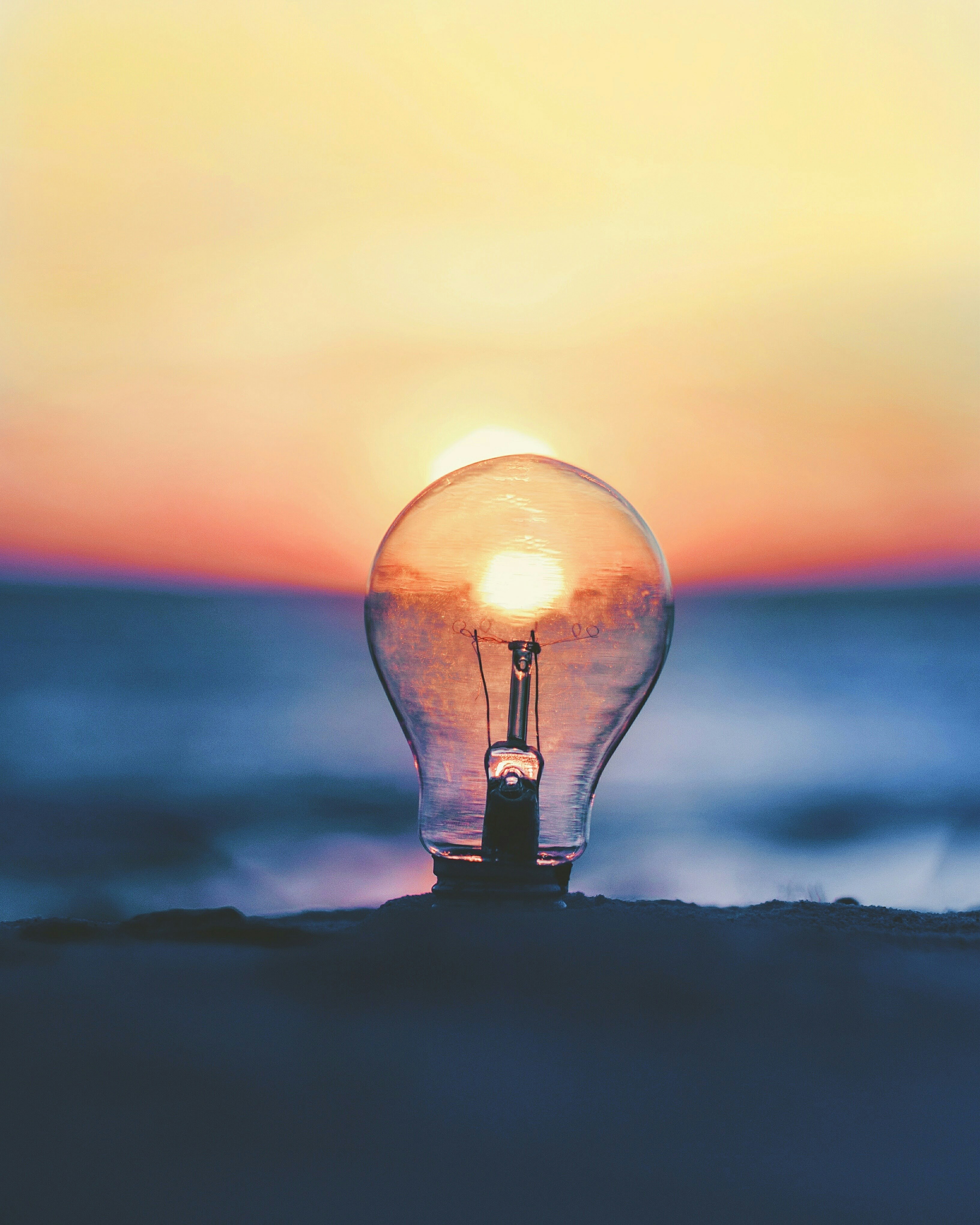 Looking through a light bulb on the beach with water behind and the sun replacing the light of the light bulb